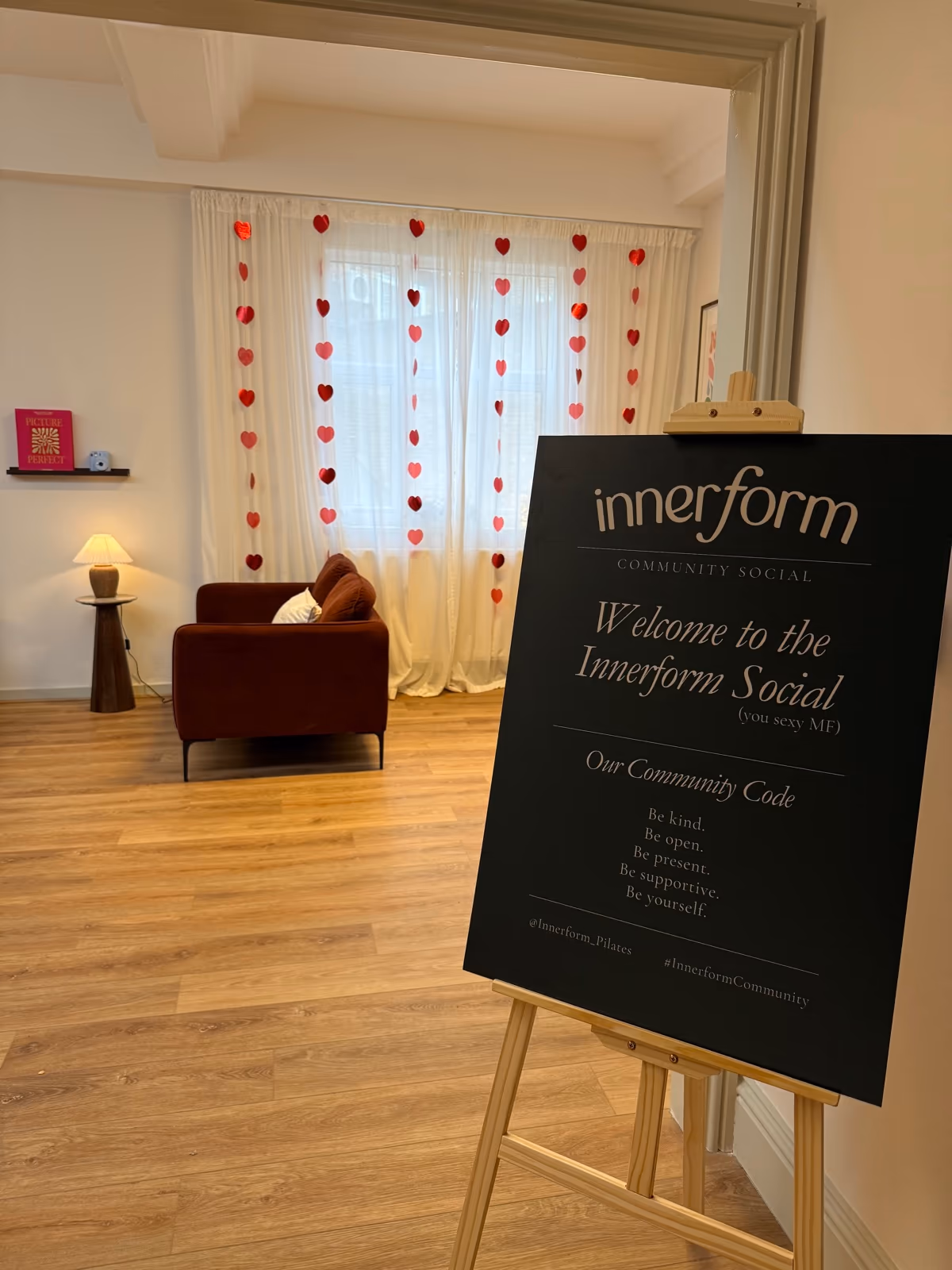 The communal area at Innerform set up for an Innerform Social - welcome easel, heart-string backdrop, low seating, refreshments to one side.