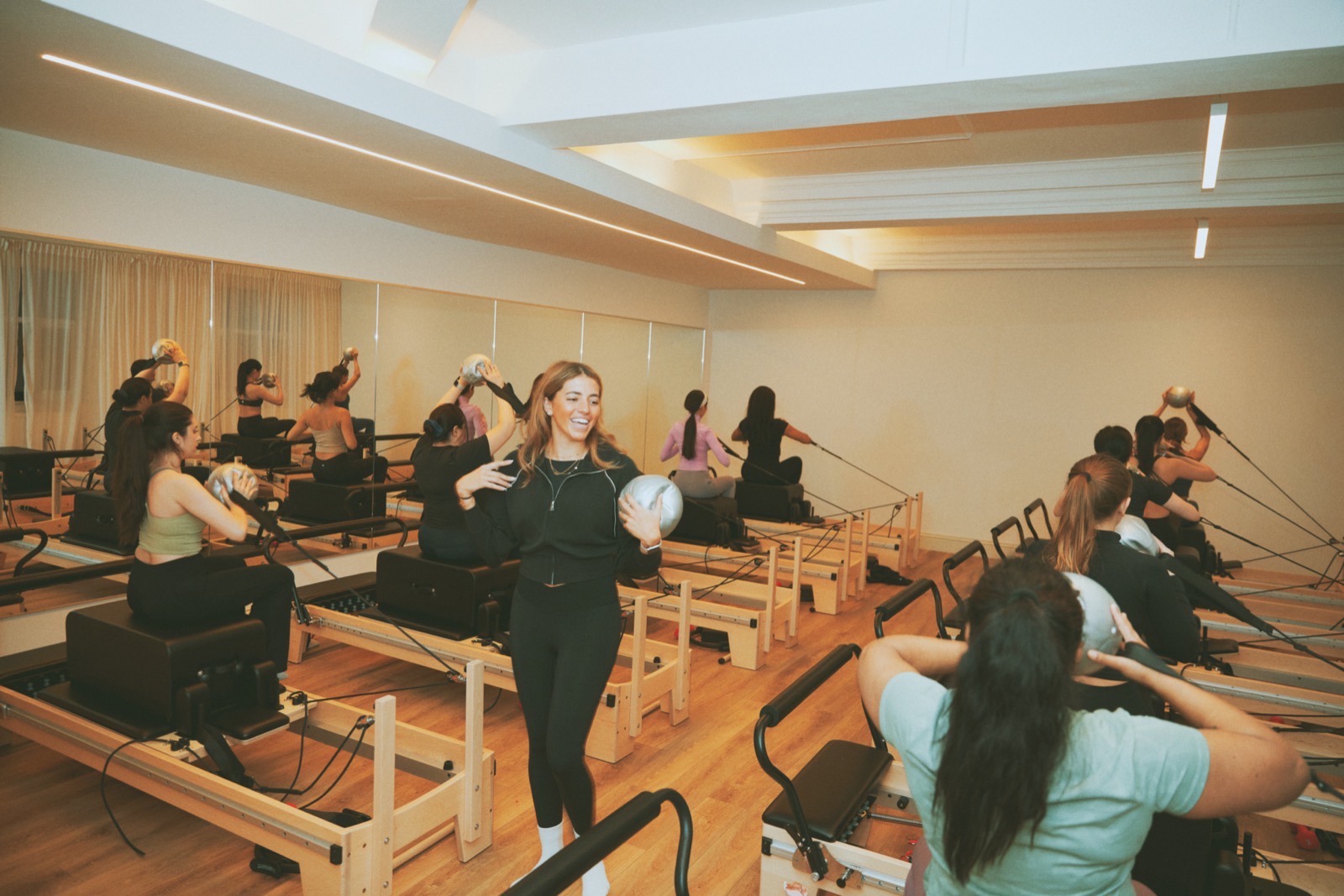A Reformer Pilates class at Innerform's Lewisham studio - members on the reformers, a teacher checking form mid-class.